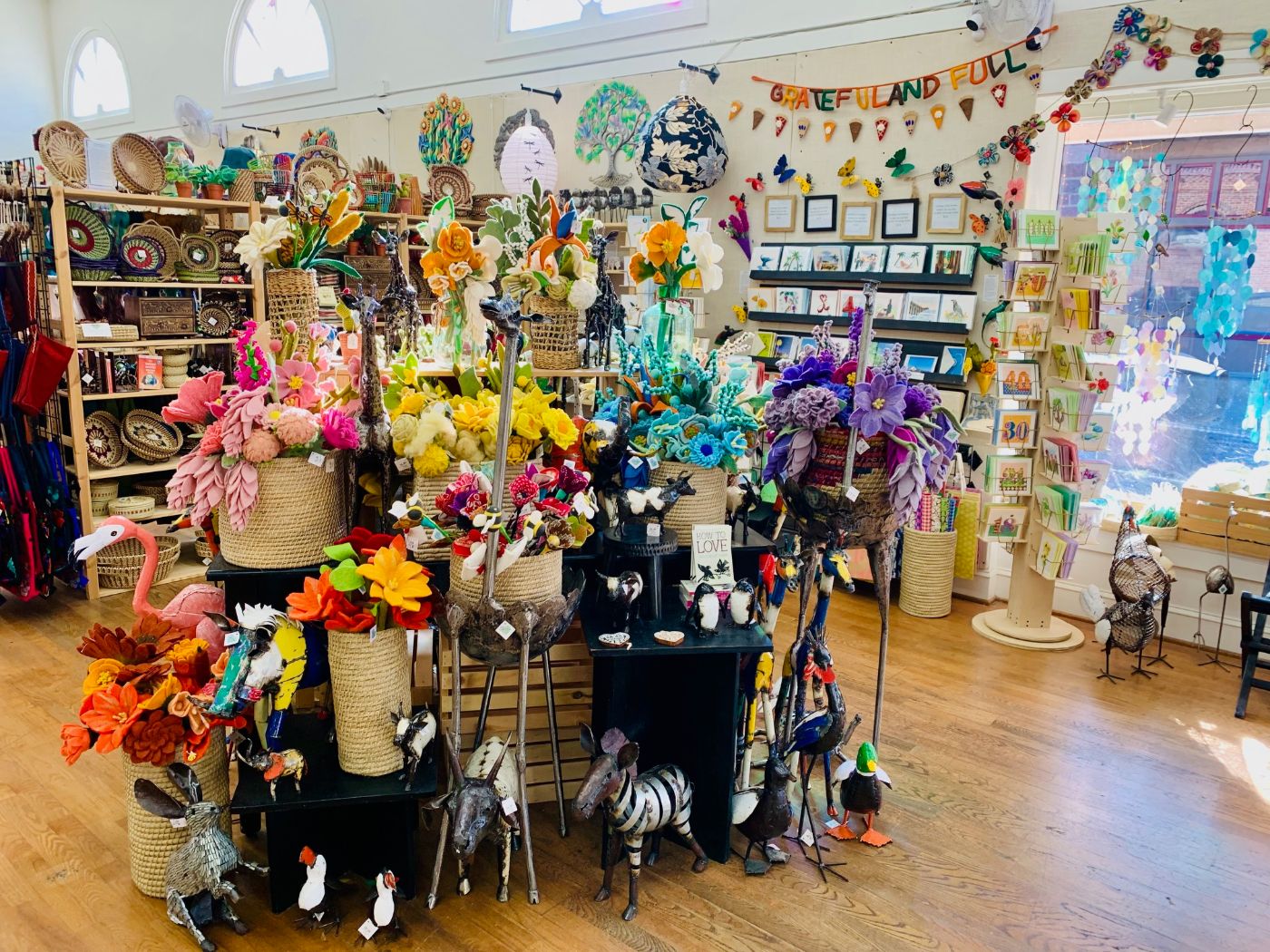 Inside Global Heart: a table of bright felt flowers in baskets and painted metal birds, in front of shelves of cards and wall art